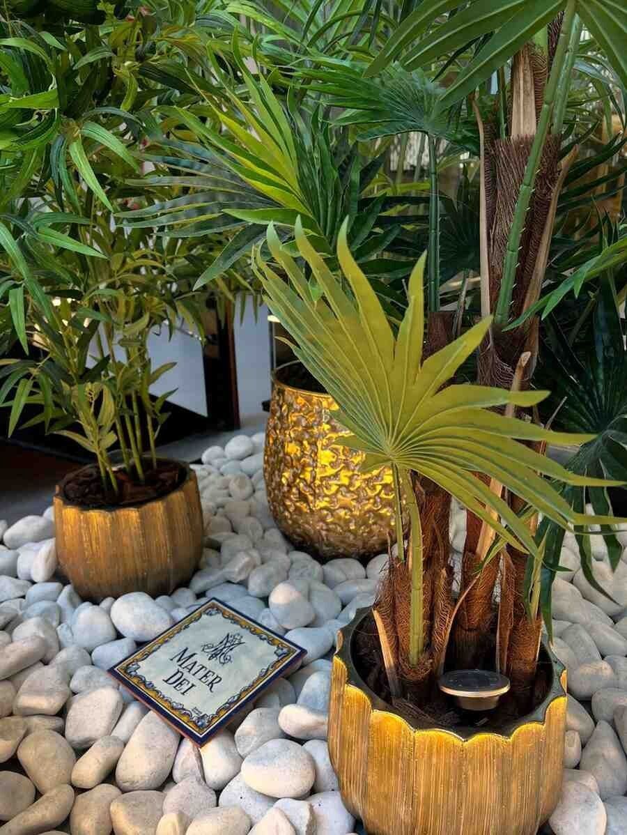 Jardineras doradas con palmeras sobre piedras blancas