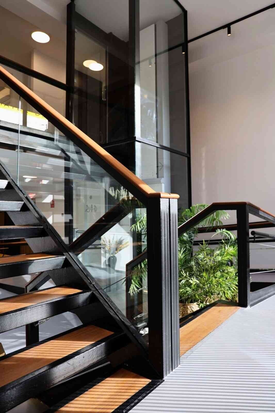 Escalera de peldaños de madera y barandilla negra junto al ascensor de cristal
