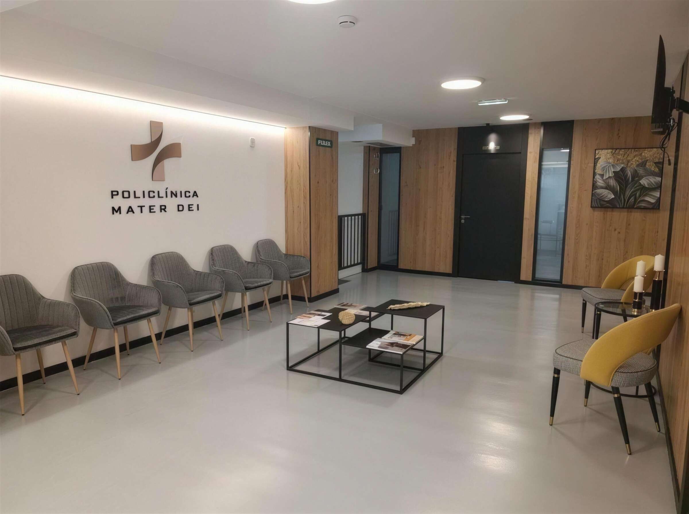 Sala de espera luminosa de Policlínica Mater Dei en Oviedo, con el logotipo en la pared, sillones y mesa baja