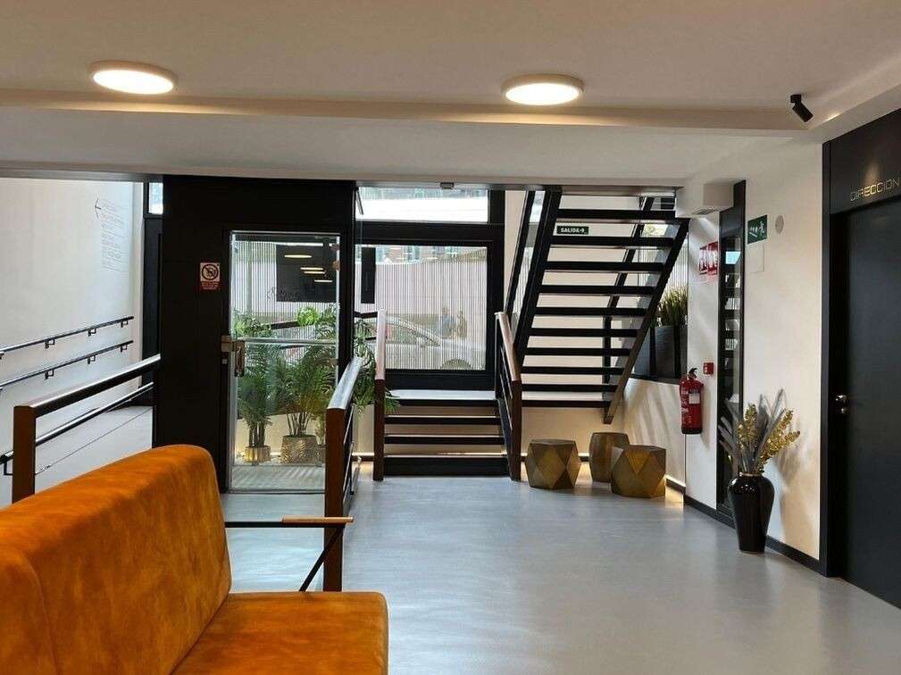 Vestíbulo con sofá mostaza, madera y escalera de acero