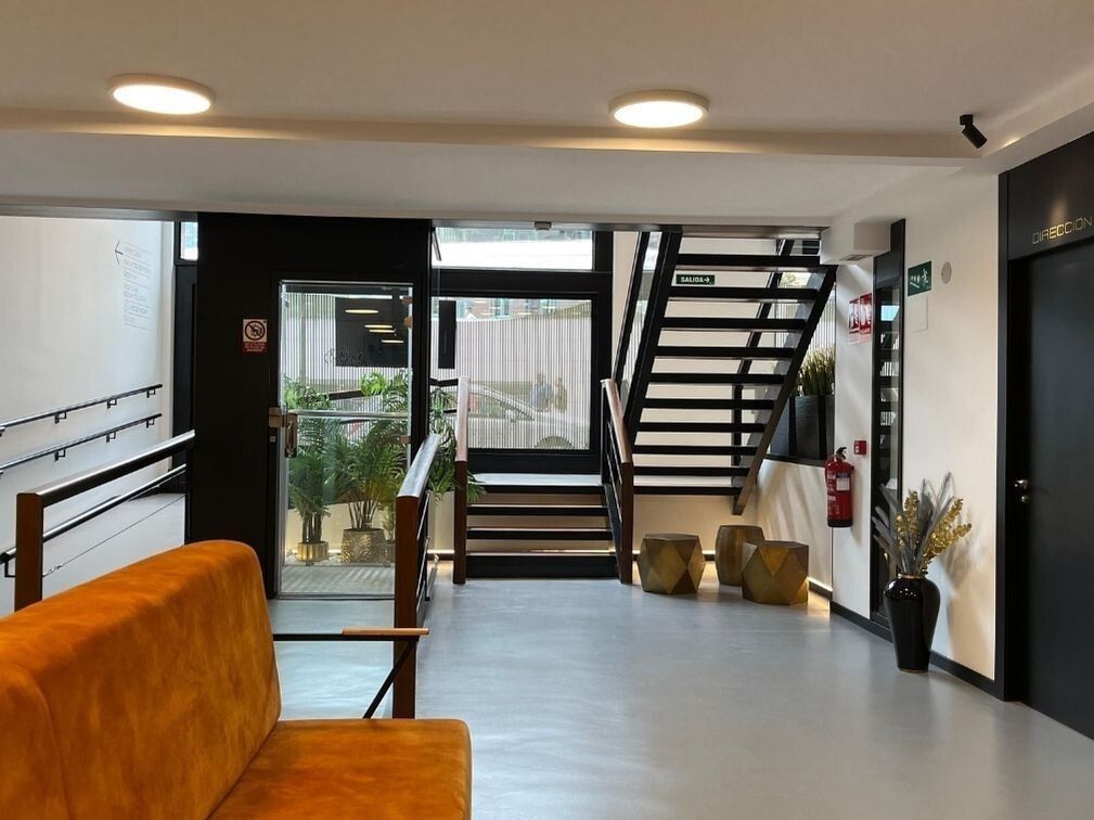 Vestíbulo luminoso con sofá mostaza, paneles de madera y escalera de acero